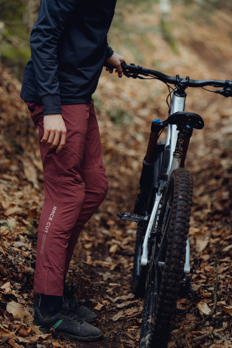Model trägt schwarzen Hoodie und Rote Hose und steht neben seinem Fahrrad