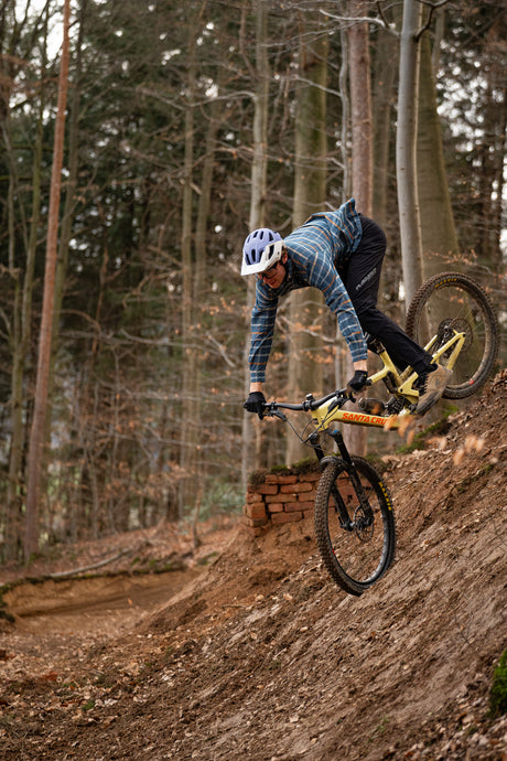 Mountainbiker in blaukariertem Hemd fährt Abhang herunter