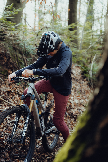 Model trägt schwarzen Hoodie und Rote Hose und sitzt auf Silbernen MTB