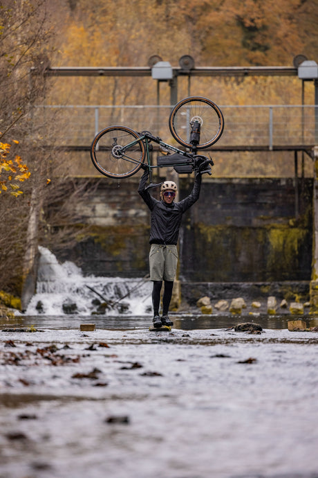 Teamfahrer Stephan Peters steht im Bach und hält Fahrrad über dem Kopf